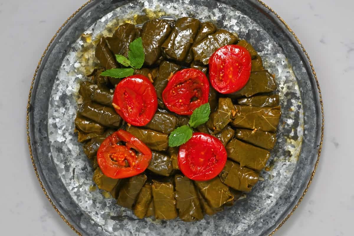 Dolmas on a platter topped with mint leaves and tomatoes