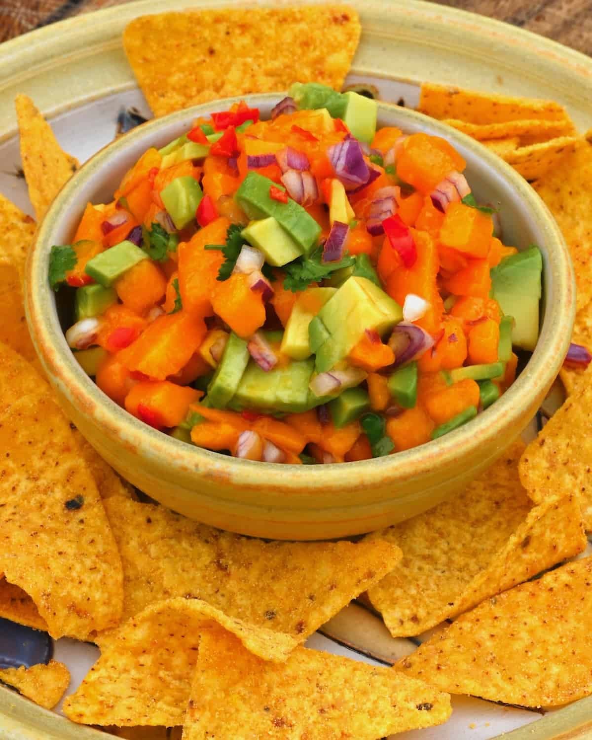 A small bowl with mango salsa with tortilla chips around it