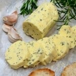 Homemade garlic butter cut into slices with garlic cloves next to it - 17