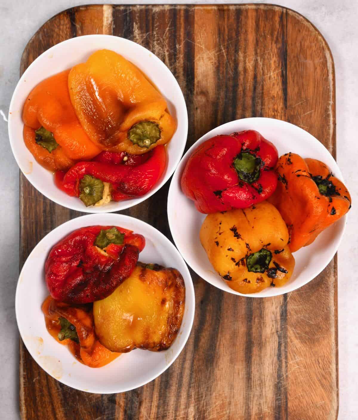 Three bowls with roasted bell peppers on a chopping board