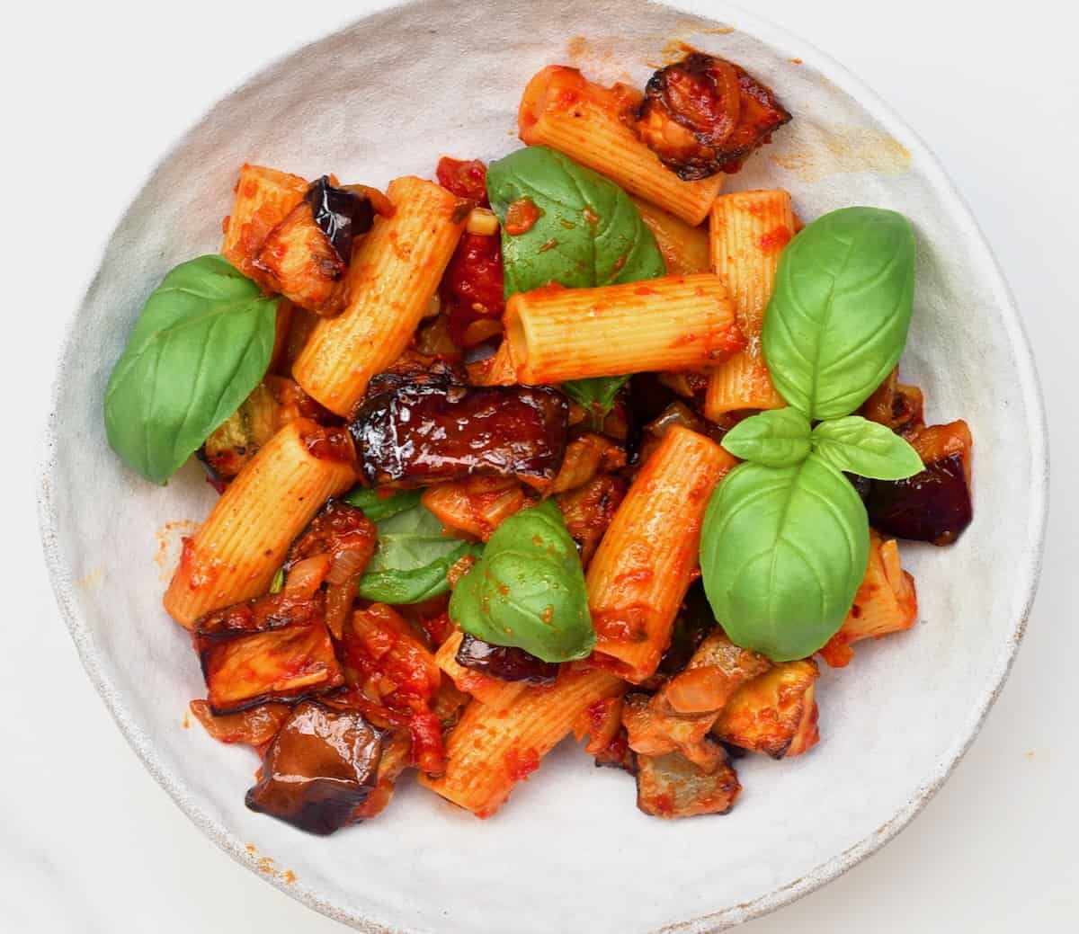 A serving of Pasta Alla Norma topped with fresh basil leaves