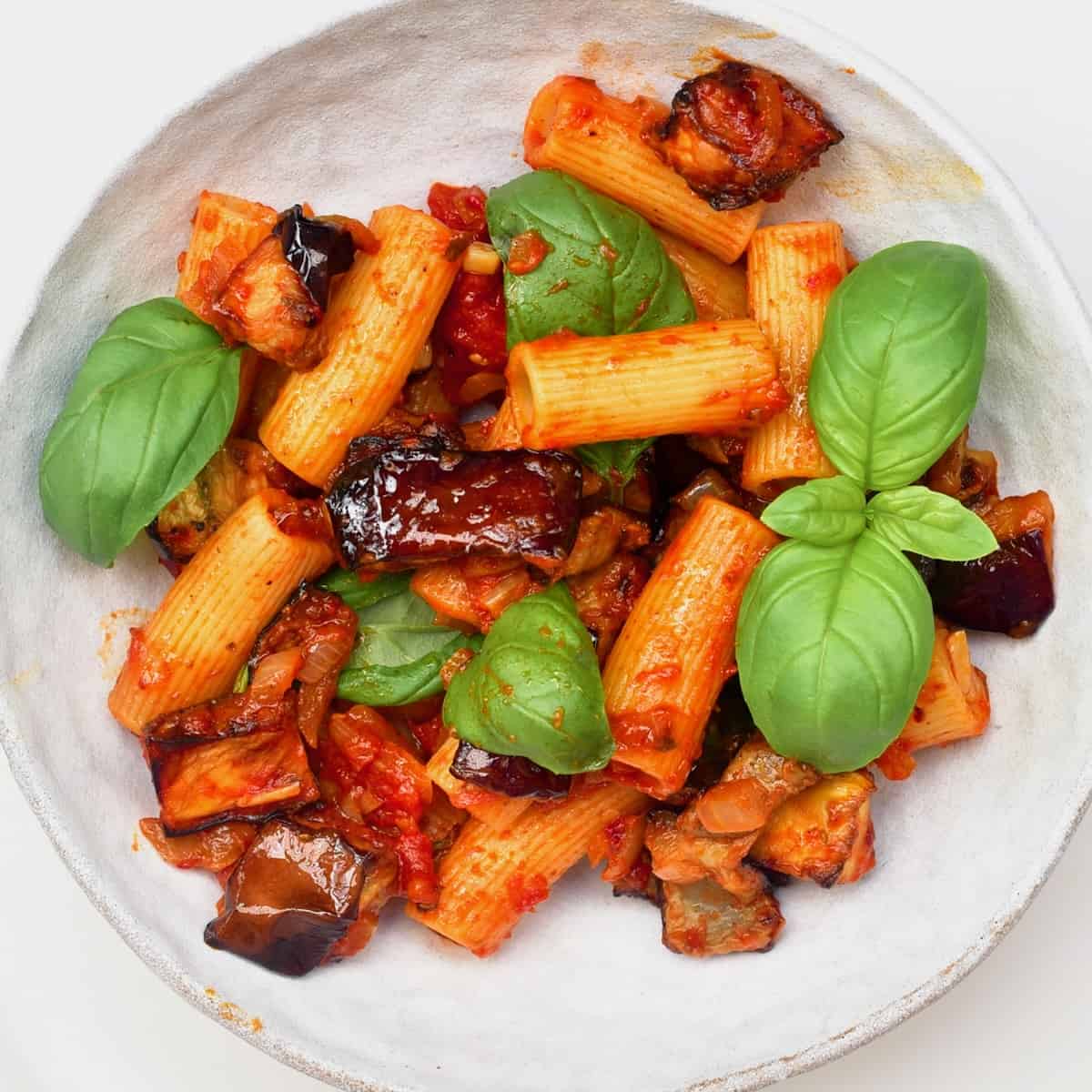 A serving of Pasta Alla Norma topped with fresh basil leaves