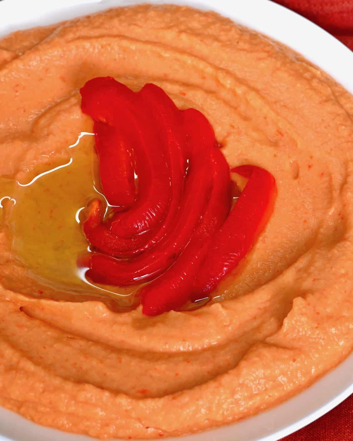 A bowl with roasted red pepper hummus topped with a few red pepper slices
