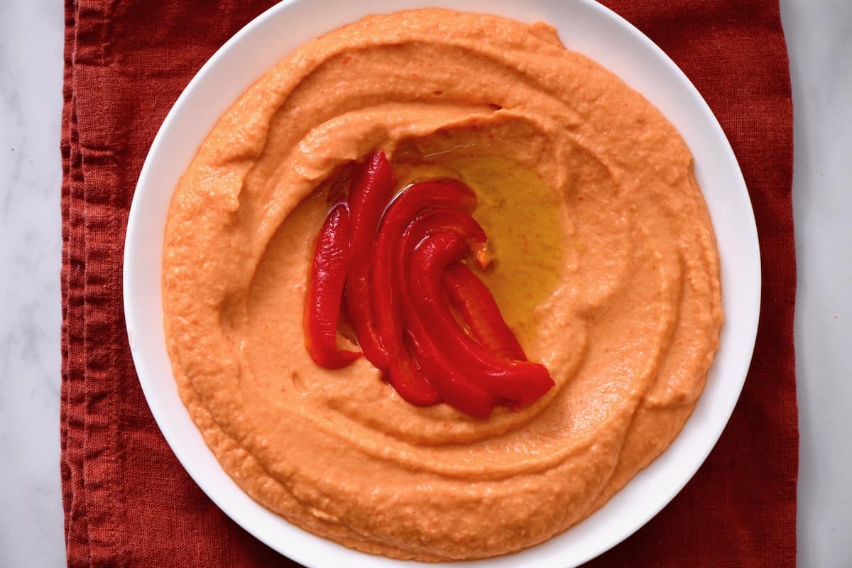 A bowl with homemade roasted red pepper hummus topped with a few red pepper slices