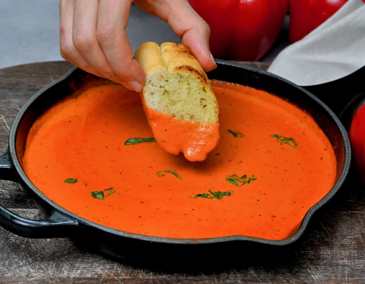 Dipping garlic bread into roasted red pepper sauce