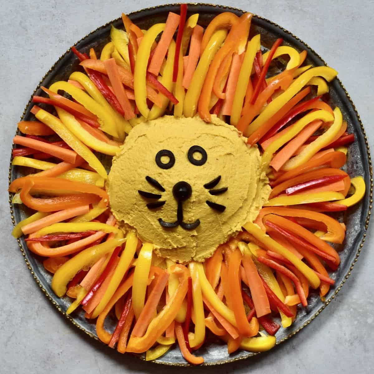 Pumpkin hummus served with bell pepper slices and olives organized as lion's face