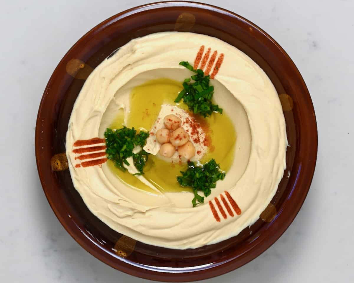 A bowl with homemade hummus topped with olive oil, paprika, chickpeas, and parsley