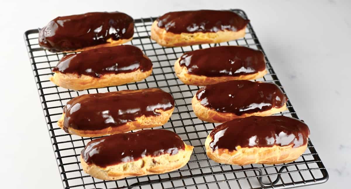Eight homemade chocolate eclairs on a cooling rack