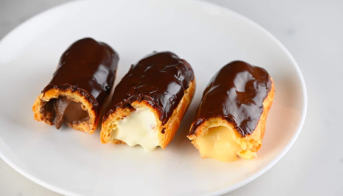 Three half eaten eclairs with different fillings - chocolate, whipped cream, and vanilla custard