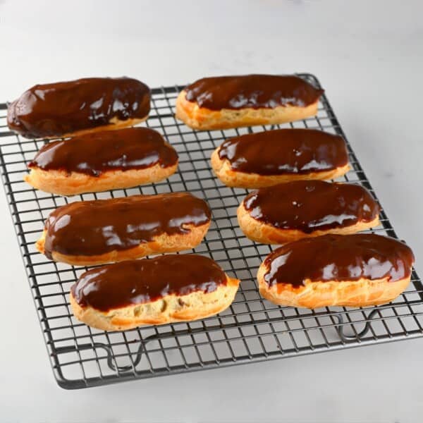 Eight homemade chocolate eclairs on a cooling rack