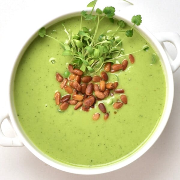 A bowl with pea soup topped with toasted pine nuts
