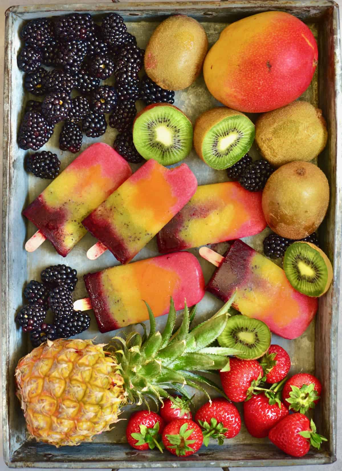 A tray filled with berries, mango, kiwi, pineapple, and homemade fruit popsicles