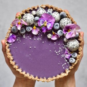 A blueberry tart topped with edible flowers and dragon fruit pearls