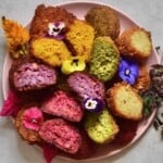 A plate with differently colored homemade falafel topped with a few edible flowers