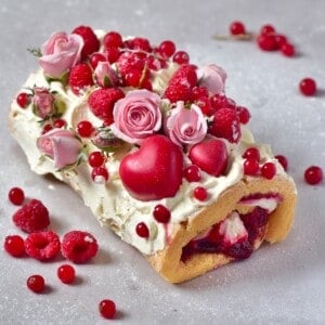 Swiss roll cake topped with red berries, mini roses, and a heart chocolate heart
