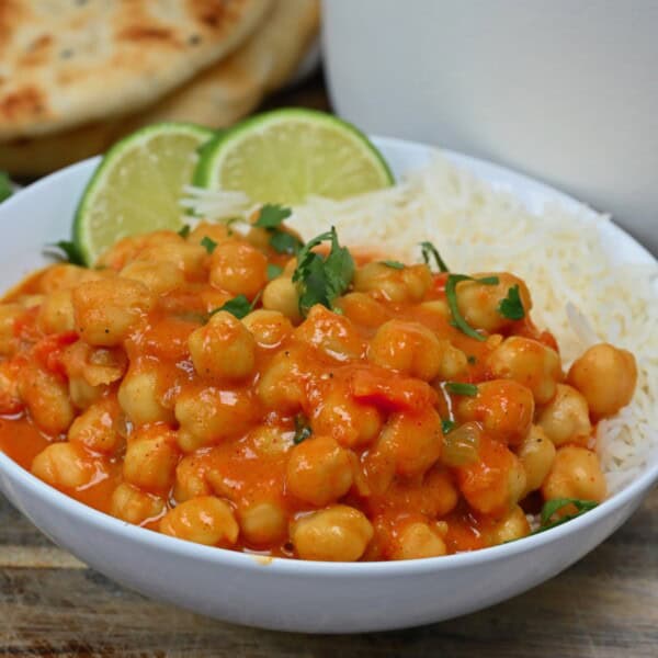 A serving of chickpea curry over rice topped with cilantro and lime