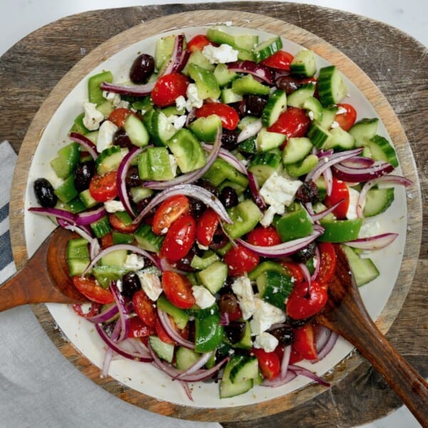 A large bowl with tossed greek salad topped with red onion and olives
