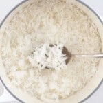 A spoonful of jasmine rice over rice in a saucepan.