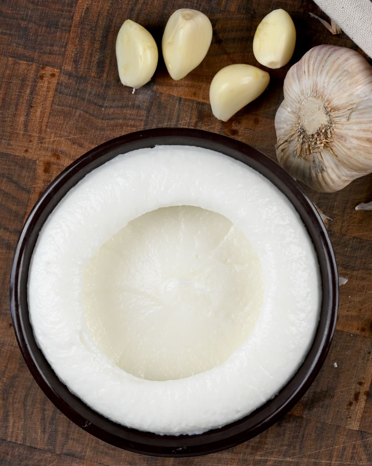 Homemade Lebanese garlic sauce in a small bowl with a few garlic cloves around it.