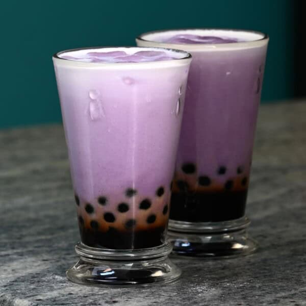 Two tall glasses with freshly made taro milk tea with tapioca pearls.