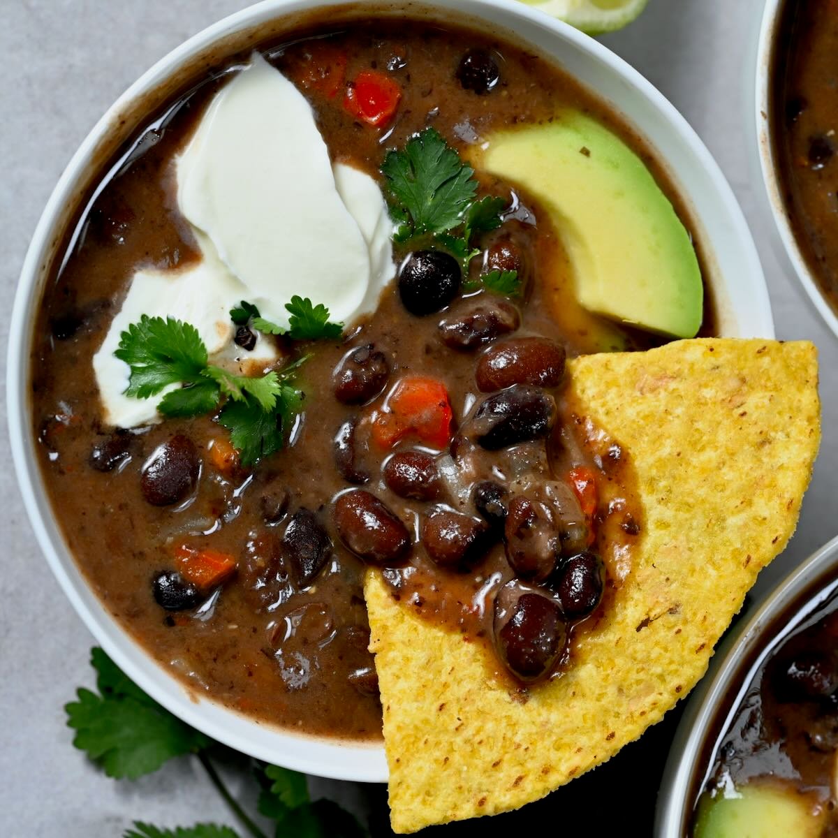 A small bowl of black bean soup topped with tortilla chip, sliced avocado, and sour cream. - 37