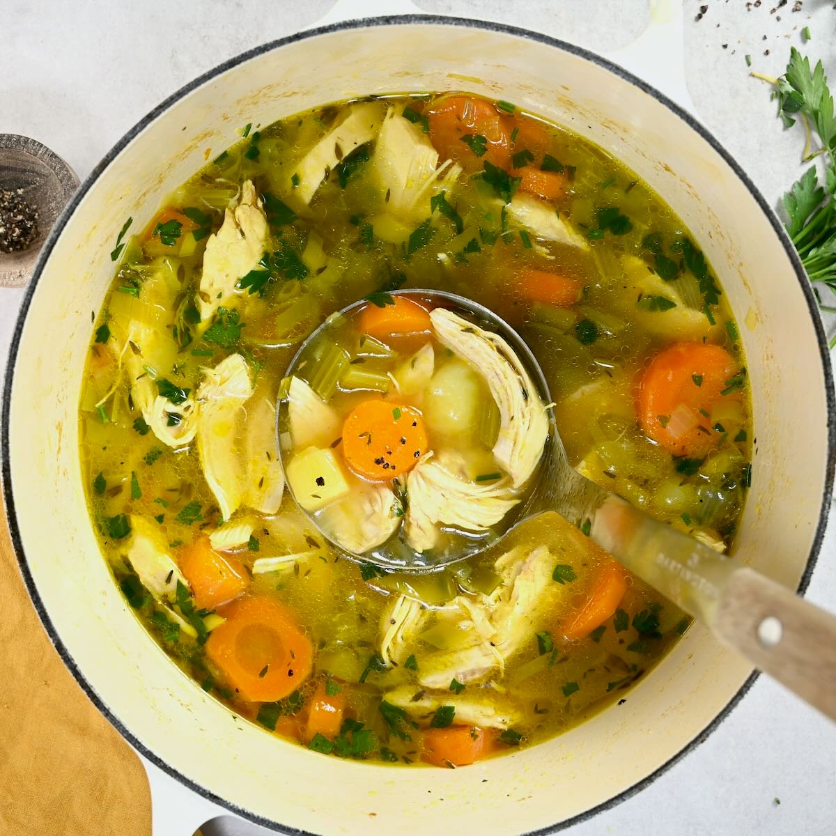 A large pot with homemade chicken soup and a ladle. - 13