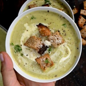 A serving of zucchini soup topped with croutons and extra cheese.