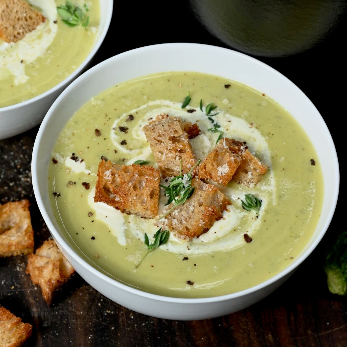 A serving of zucchini soup topped with croutons, cracked pepper, and fresh thyme. - 55