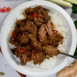 A serving of beef rendang over rice on a white plate with a fork. - 16