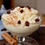 A glass serving bowl with rice pudding topped with raisins. - 13