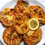 Cauliflower steaks served on a plate with a lemon slice.