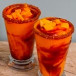 Two tall glasses filled with homemade mangonada, topped with tajin and mango chuncks. - 10