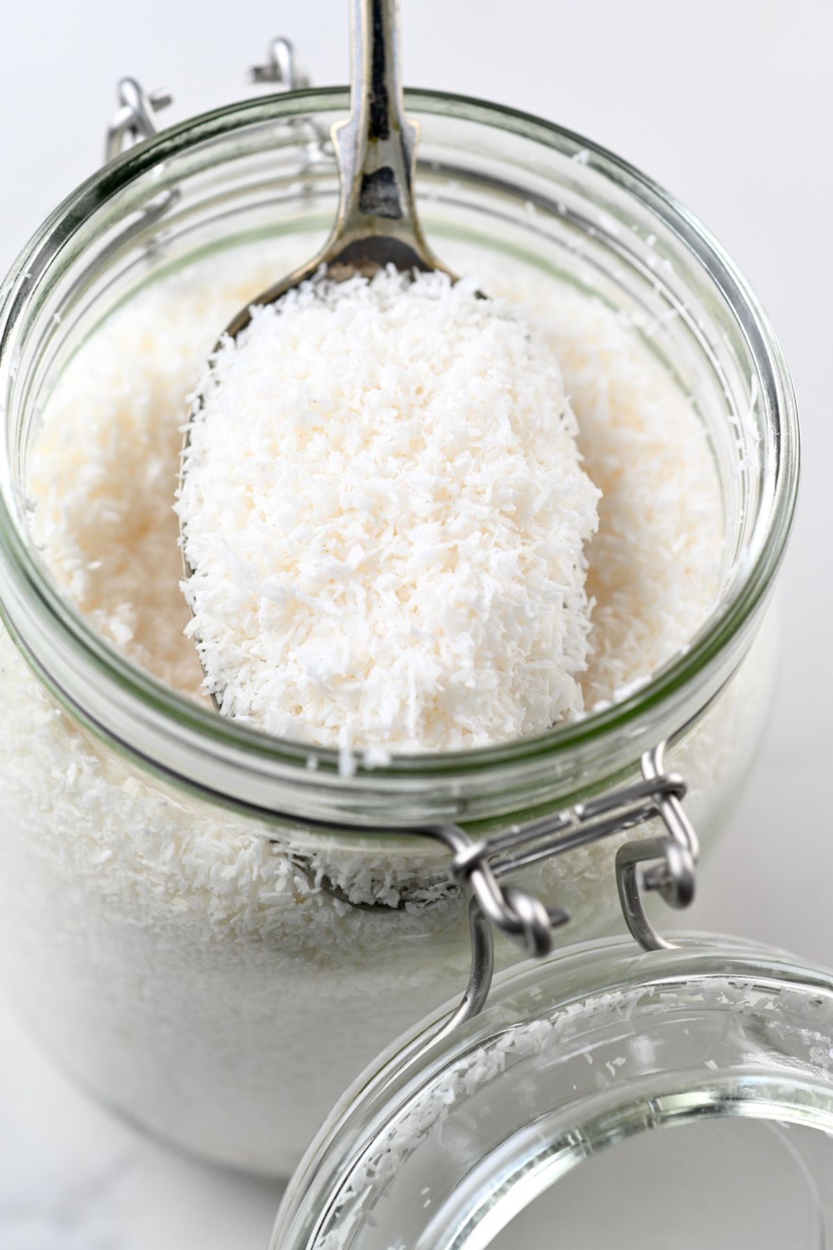 A jar filled with homemade desiccated coconut and a spoon in it.
