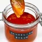 A spoon dripping dandelion honey over a jar filled with the vegan honey.