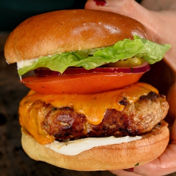 A close up square photo of a grilled burger with the cheese meltind down it.