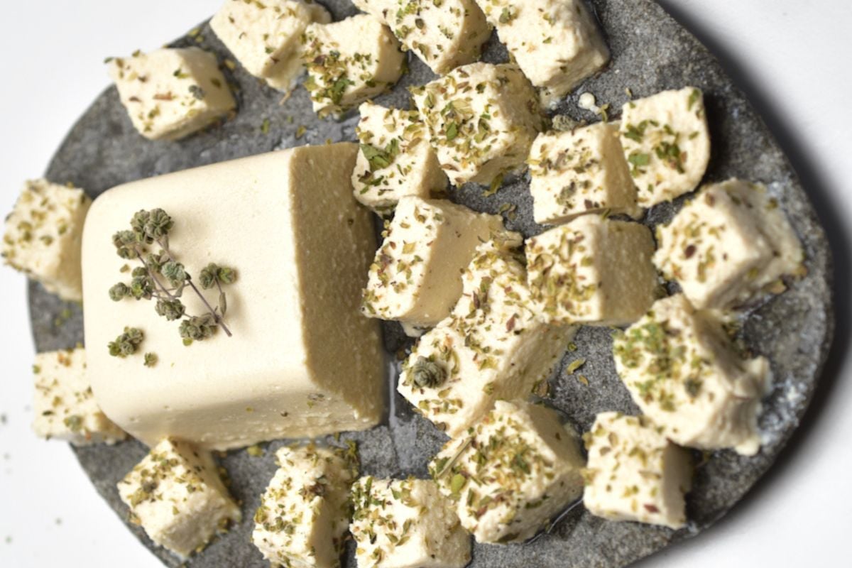 Vegan feta cheese block, partially cut into cubes and garnished with ground thyme