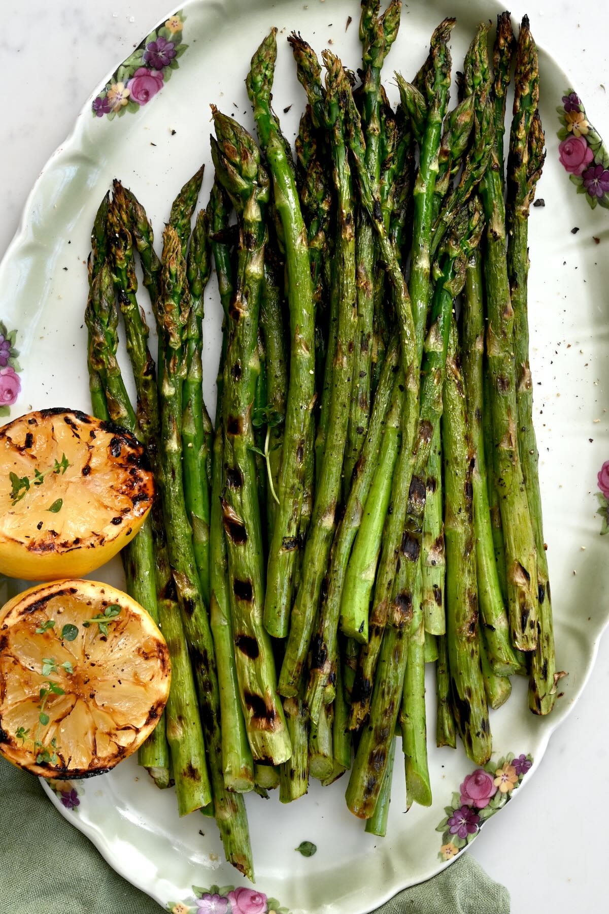 Top view of grilled asparagus on a light green plate with two halves of grilled lemons.