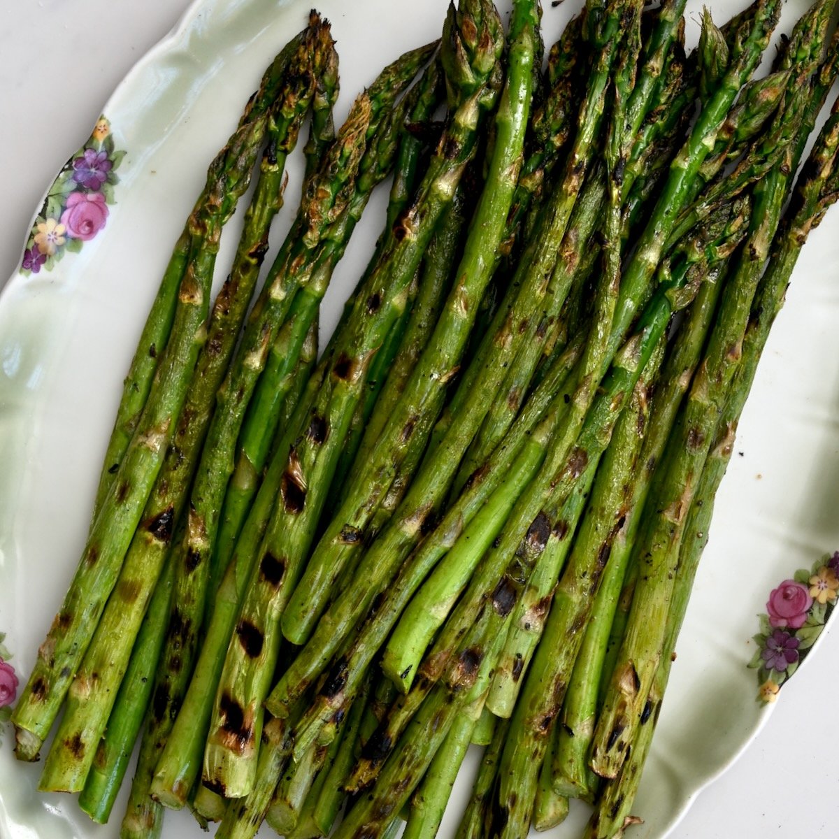 Close-up square photo of grilled asparagus on a green plate.