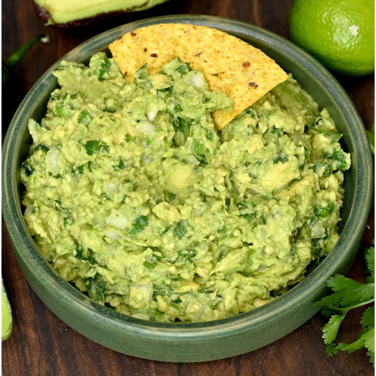 Guacamole in a green bowl with a tortilla chip dipped in.