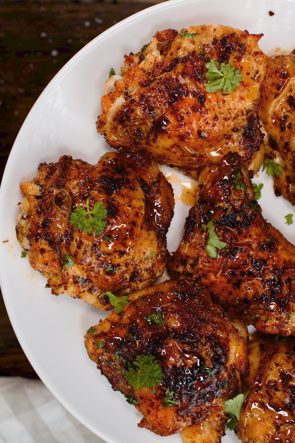 top view close up of baked chicken tips on a white plate with parsley springles on wooden board