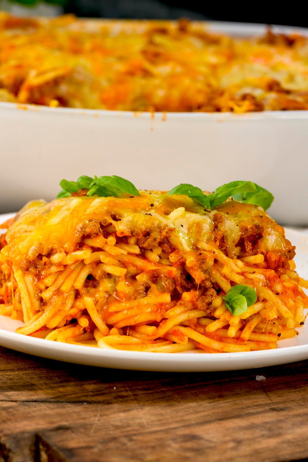 side view photo close up of baked spaghetti in a white plate with the white cassarole dish in the background