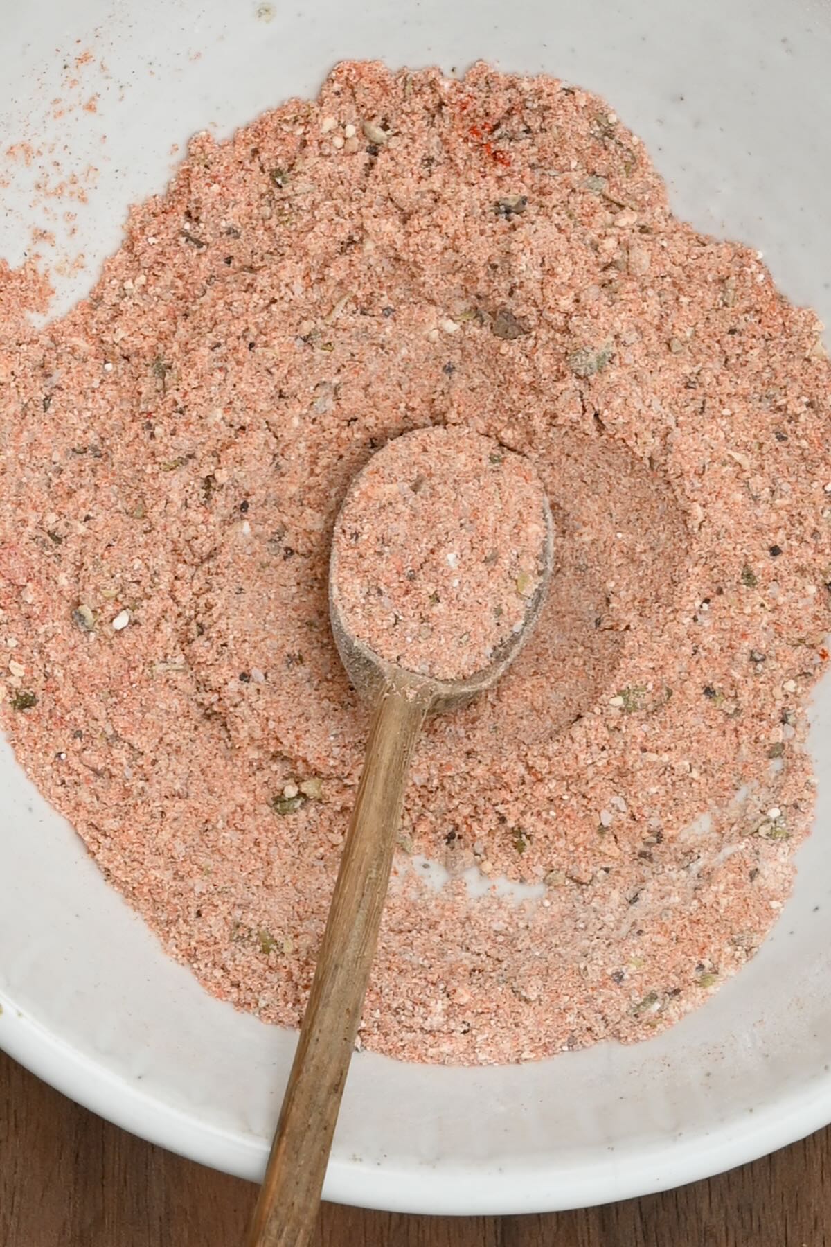 Top view close-up of blended fajita seasoning in a white plate, with some of the spice mix on a small wooden spoon.