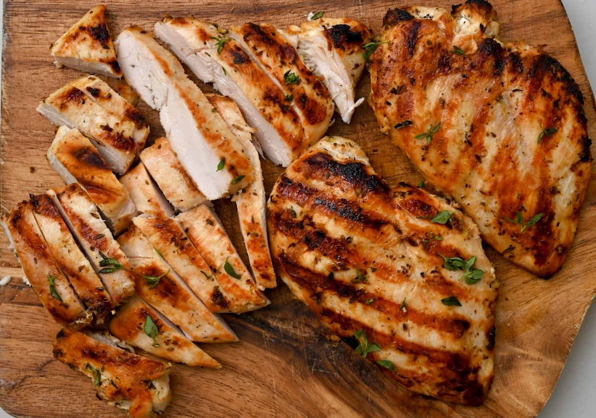 8 top view of two whole grilled chicken breasts and two sliced ones on wooden cutting board