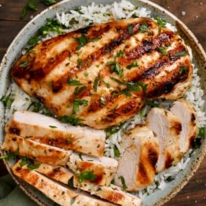 top view of grilled chicken breast in a bowl of cilantro lime rice on wooden board topped with cilantro.