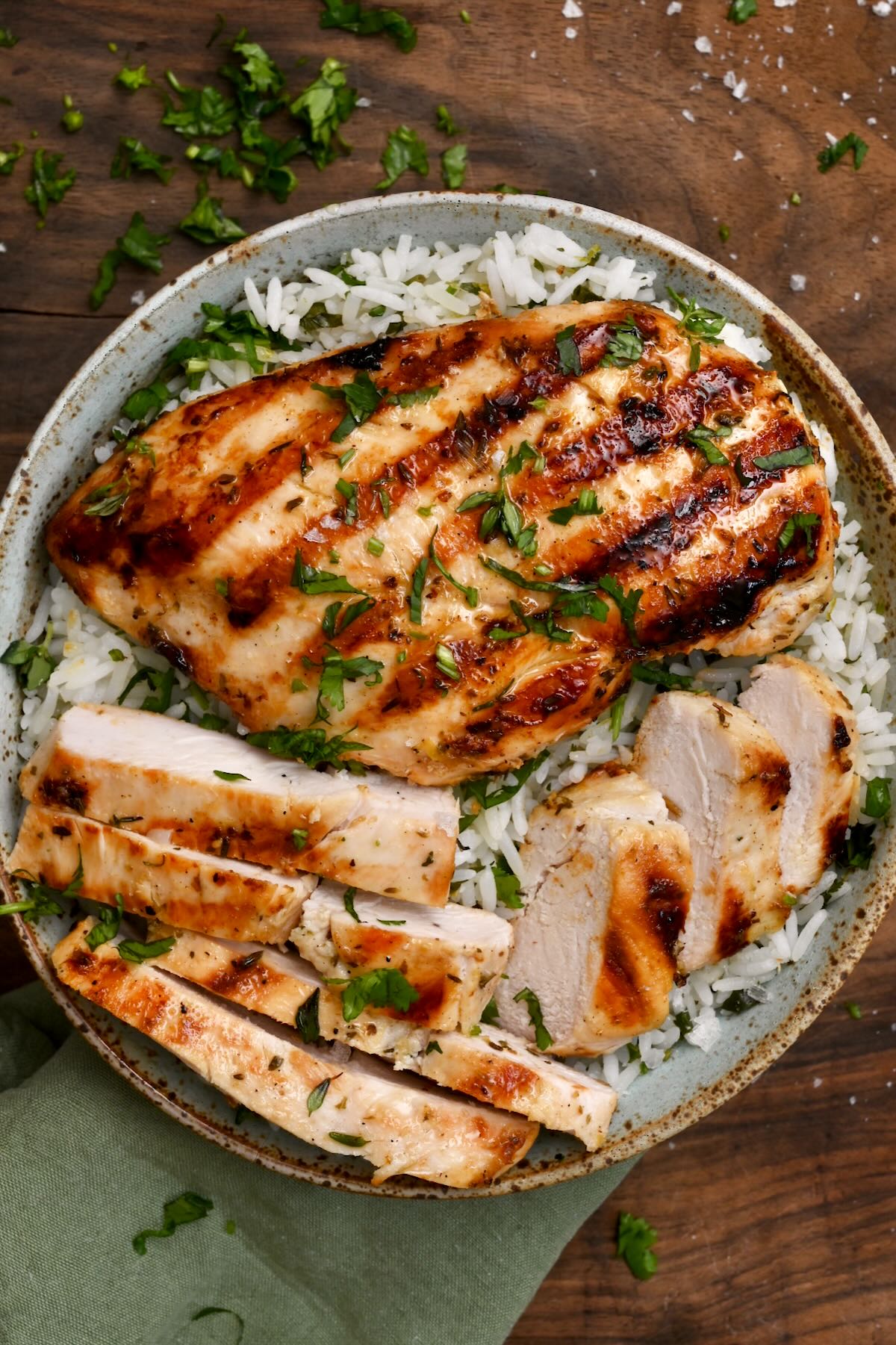 top view of grilled chicken breast in a bowl of cilantro lime rice on wooden board topped with cilantro.