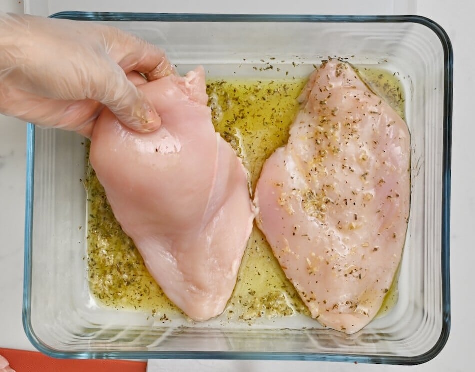 3 Hand placing raw chicken breast into marinade in a glass bowl, top view