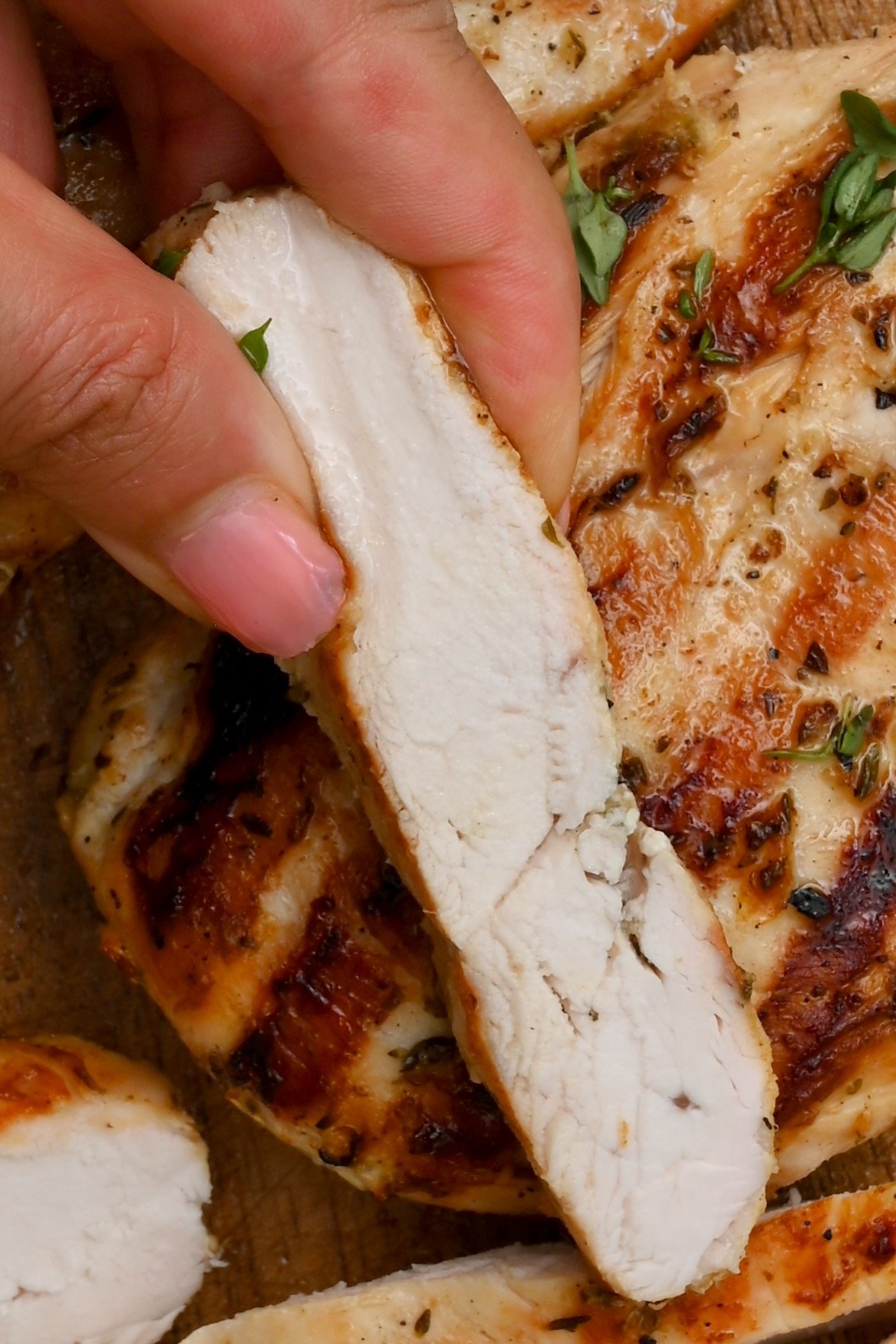 showing a slice of cut grilled chicken with some grilled chicken in the background