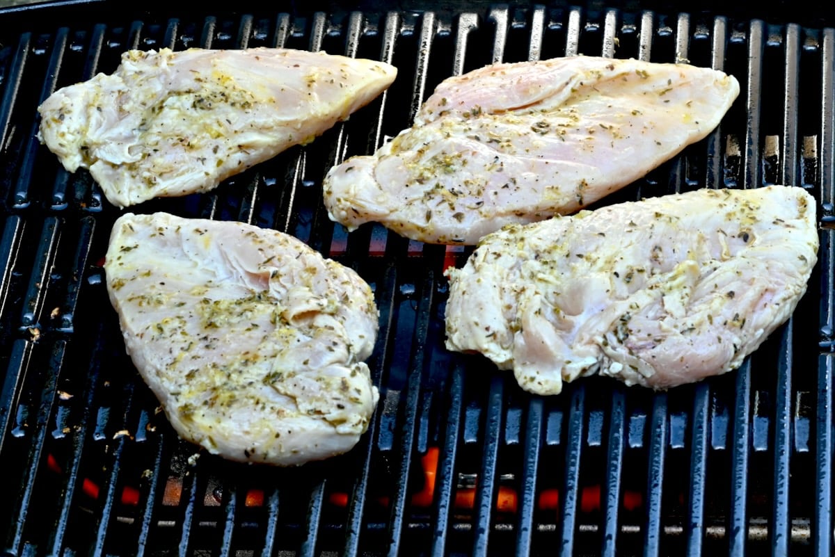 5 Four marinated chicken breasts placed on a lit grill, skin side down, side view with visible flames