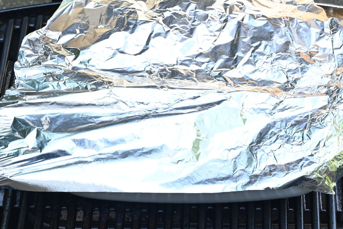 7 Tinfoil loosely covering a white container to rest grilled chicken breasts, side view