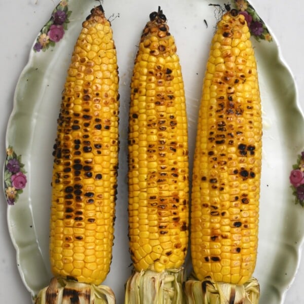 three grilled corn on the cob on a green plate